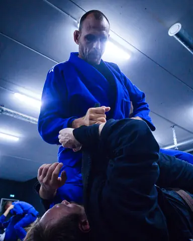 Contre-plongée sur un pratiquant en kimono bleu qui saisit le col de son partenaire allongé